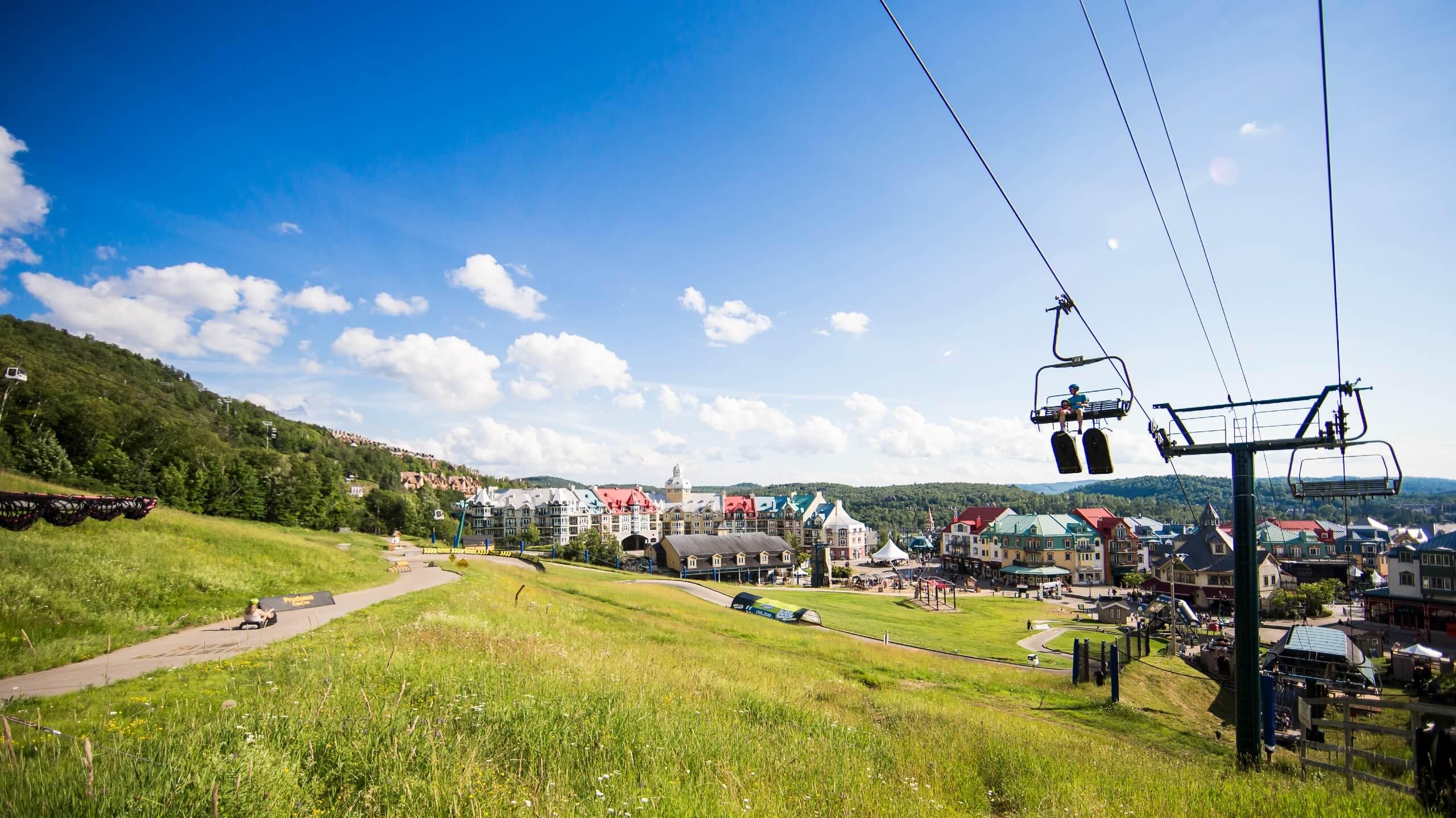 A chairlift heads to the top of the Luge tracks with a father and son with views of Mont Tremblant behind.