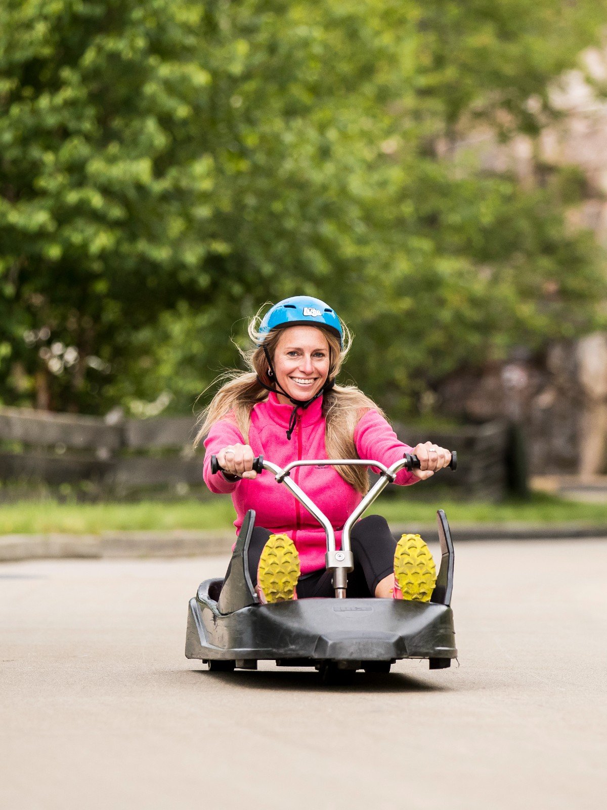 A blonde woman smiles as she rides down the Skyline Luge Mont Tremblant track.