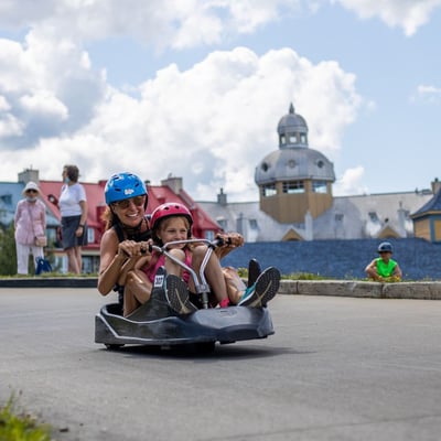 A mother rides down the Luge with her daughter in the same cart.