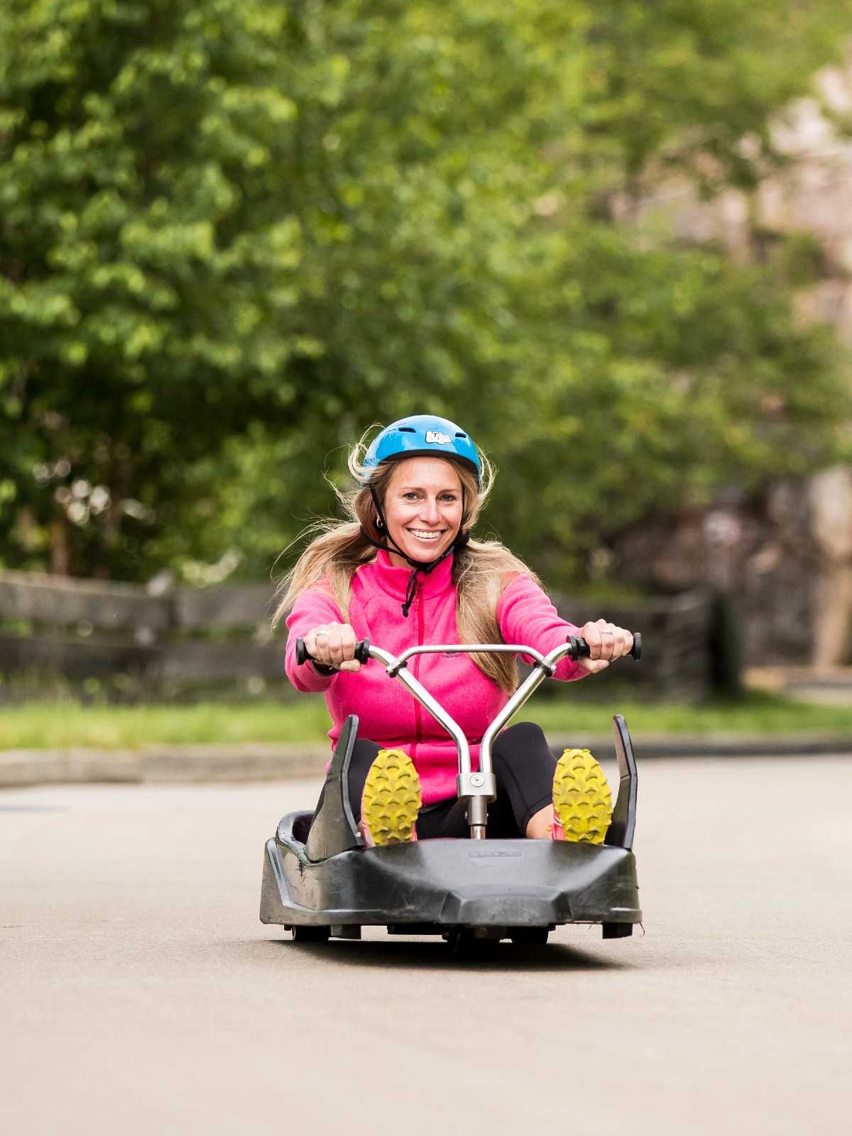 A blonde woman smiles as she rides down the Skyline Luge Mont Tremblant track.