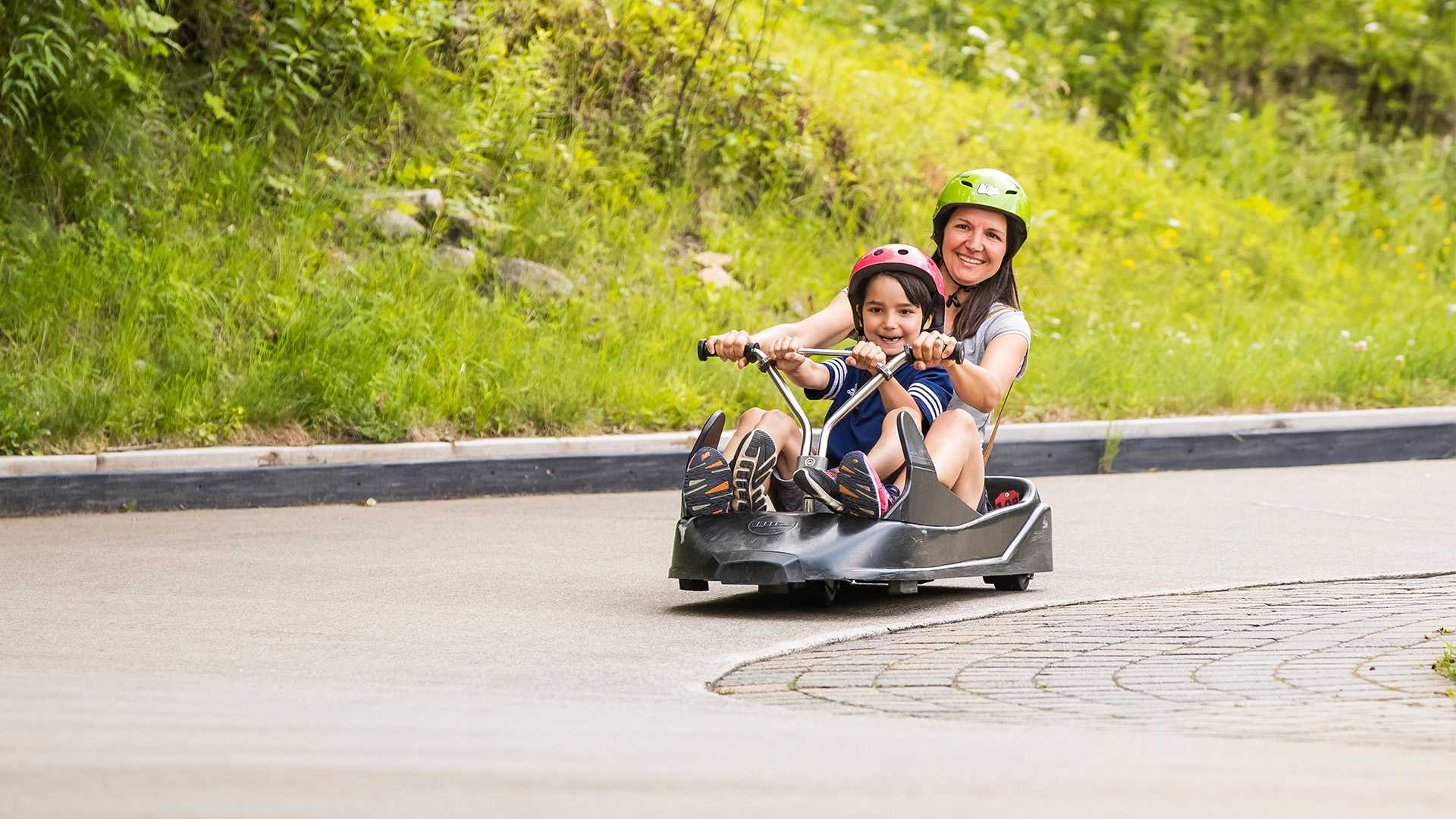 A mother and son smile as they cruise down the track at Skyline Luge Mont Tremblant.