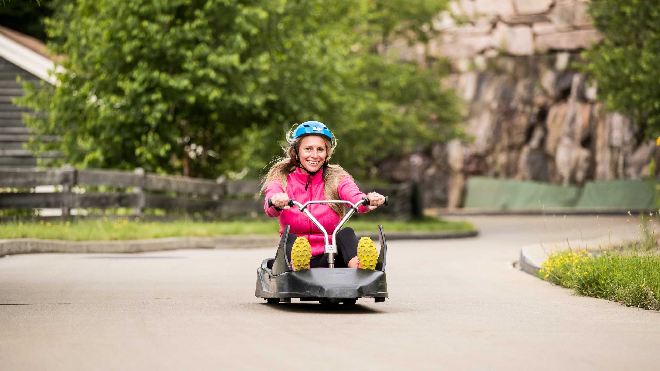A blonde woman smiles as she rides down the Skyline Luge Mont Tremblant track.